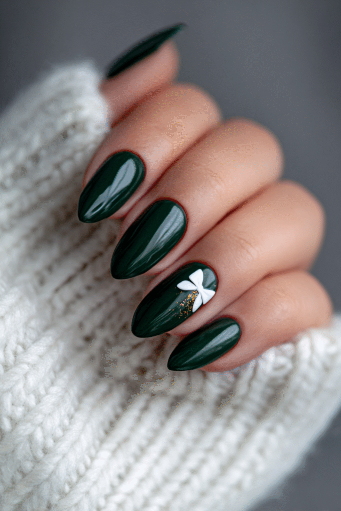 Glossy dark-green almond nails with a white bow accent and subtle gold glitter.