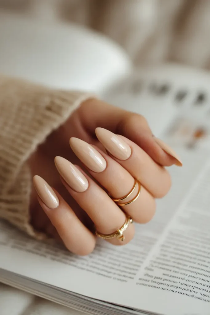 nude almond nails with a glossy finish and minimalist gold rings