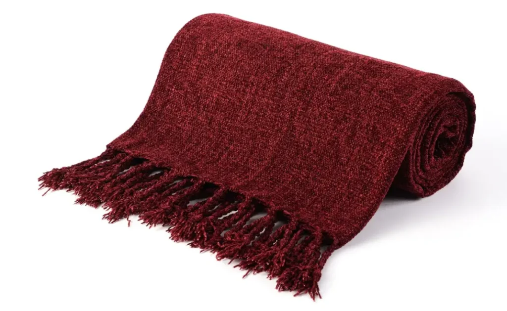 burgundy knitted throw blanket rolled with long fringe detailing on a white background