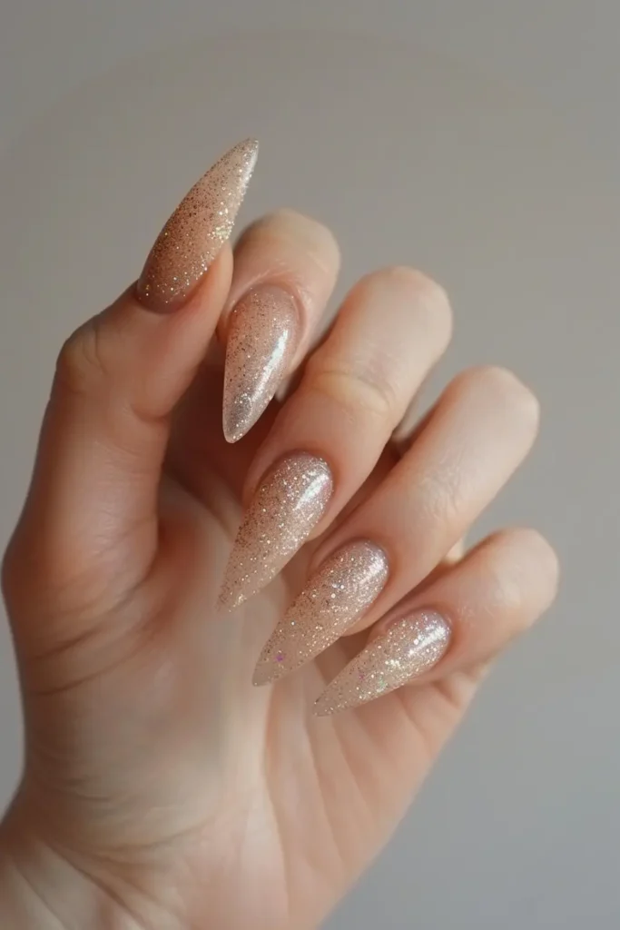 Long nude stiletto nails with gold glitter gradient, dramatic New Year’s Eve nails.