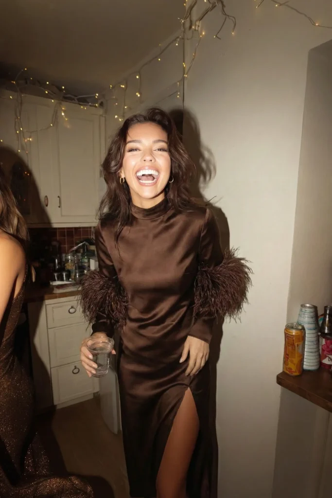 woman laughing in a brown satin dress with feather sleeves at a holiday party