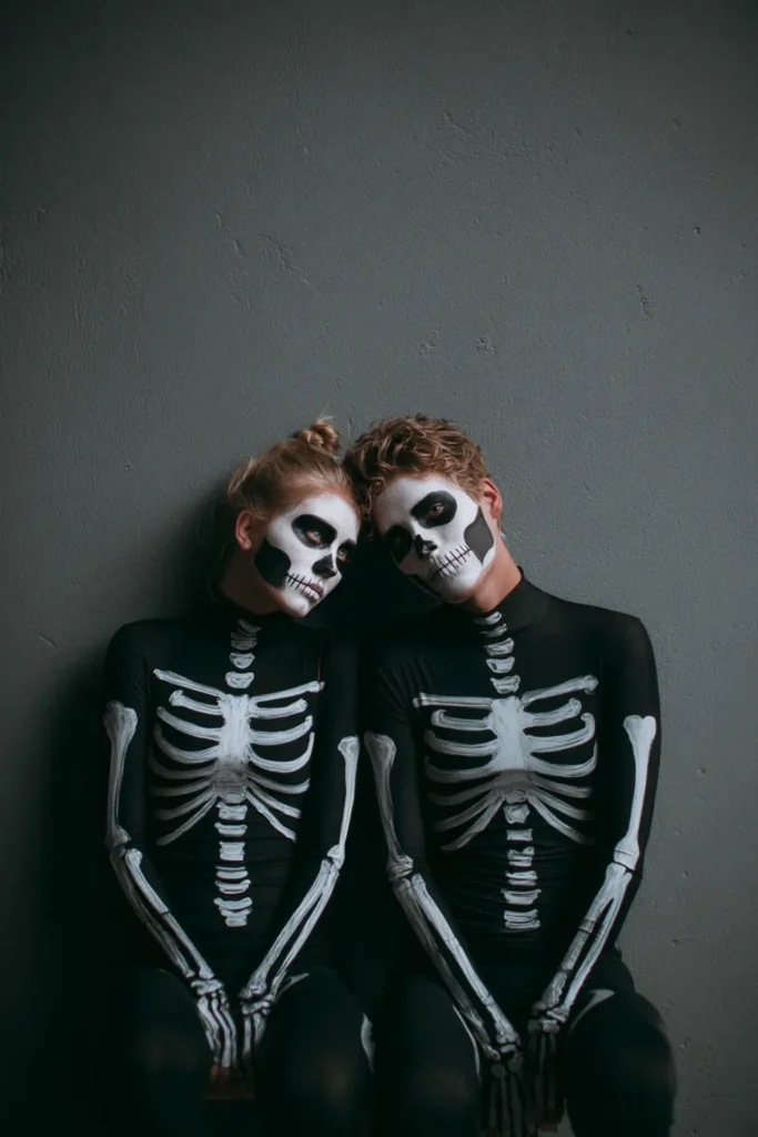 Matching skeleton body-paint Halloween couple posing together with detailed black-and-white bone designs.