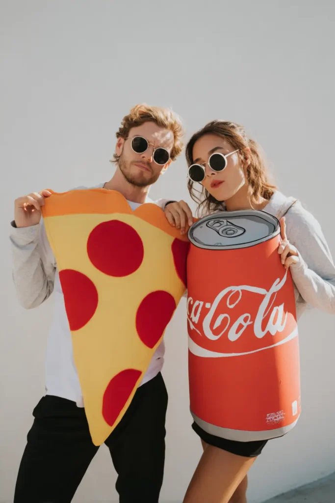 Funny Halloween couple costume with one partner dressed as a giant pizza slice and the other as a soda can.”