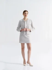 Model in a light grey tweed skirt suit with gold buttons — chic elegant outfit in a clean minimalist studio setting.