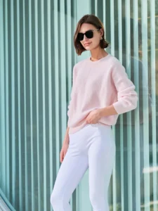 Woman wearing a soft pink sweater and white tailored pants with black sunglasses — modern minimalist street-style look.