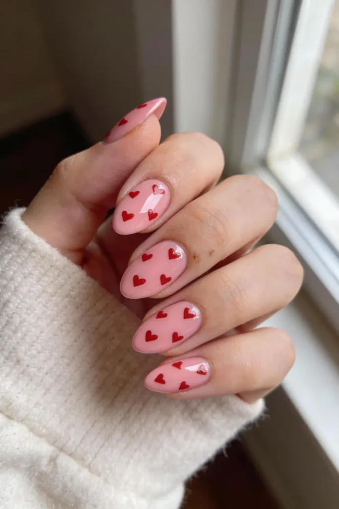 Pink almond Valentine’s Day nails with all over red heart design and glossy finish