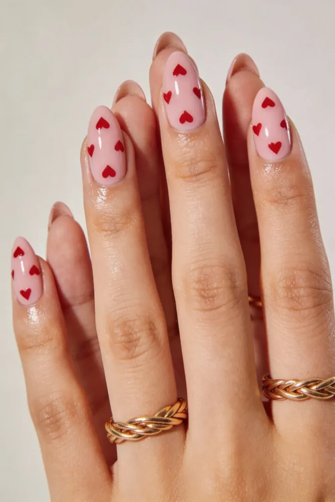 Soft pink Valentine’s Day nails with small red heart prints on almond shaped nails